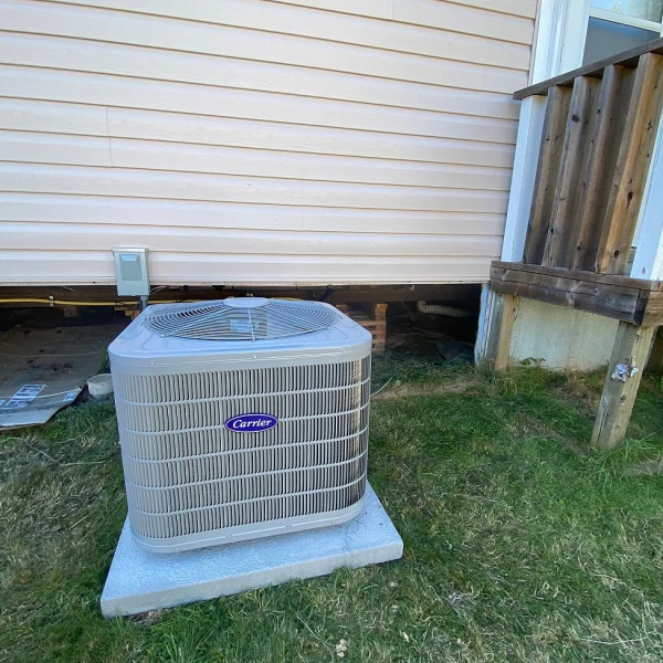 A compact Carrier brand air conditioning unit sits outside a residential home, waiting for installation